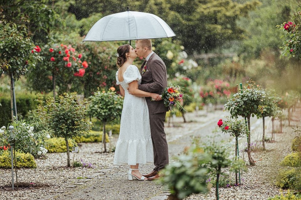 Hochzeitspaar mit Regenschirm im Regen im Rosarium in Wilhelmshaven